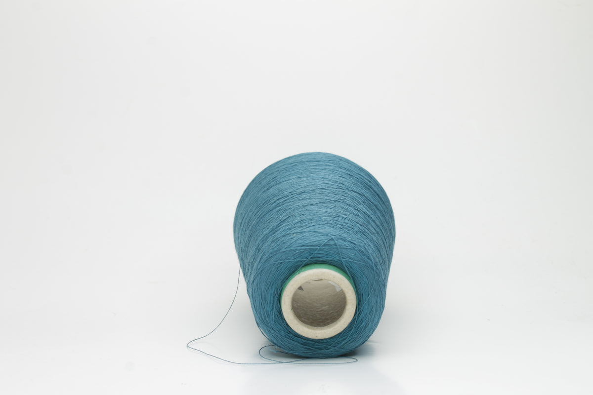 A skein of luxurious 100% pure silk yarn in a deep, shimmering petrol blue, displaying a smooth, finely spun single ply with a high, lustrous sheen.