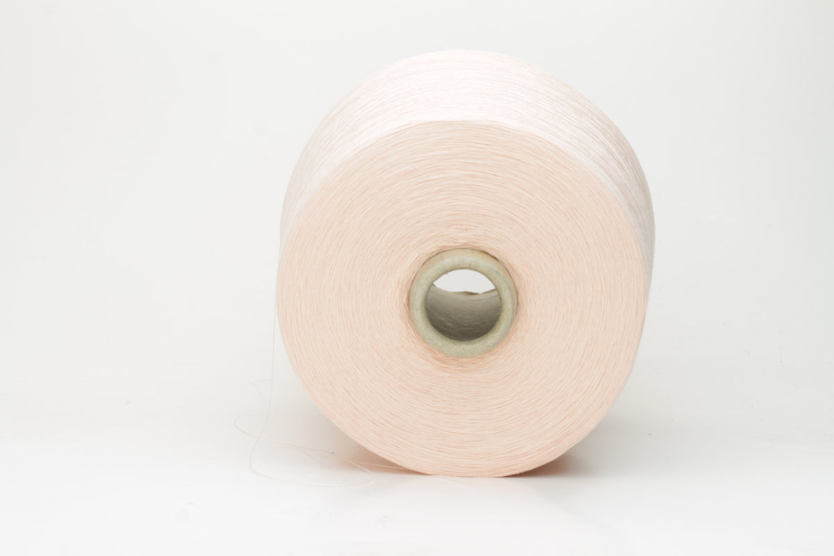 Close-up of finely spun, delicate powder pink cotton yarn, showcasing its soft, matte finish and subtle, even twist with excellent stitch definition.