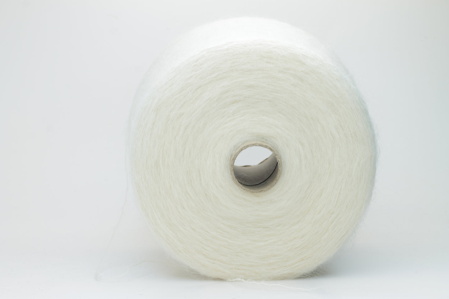 Close-up of fine white Kid Mohair and Silk yarn, exhibiting a soft, ethereal halo and subtle luminous sheen, gently twisted.