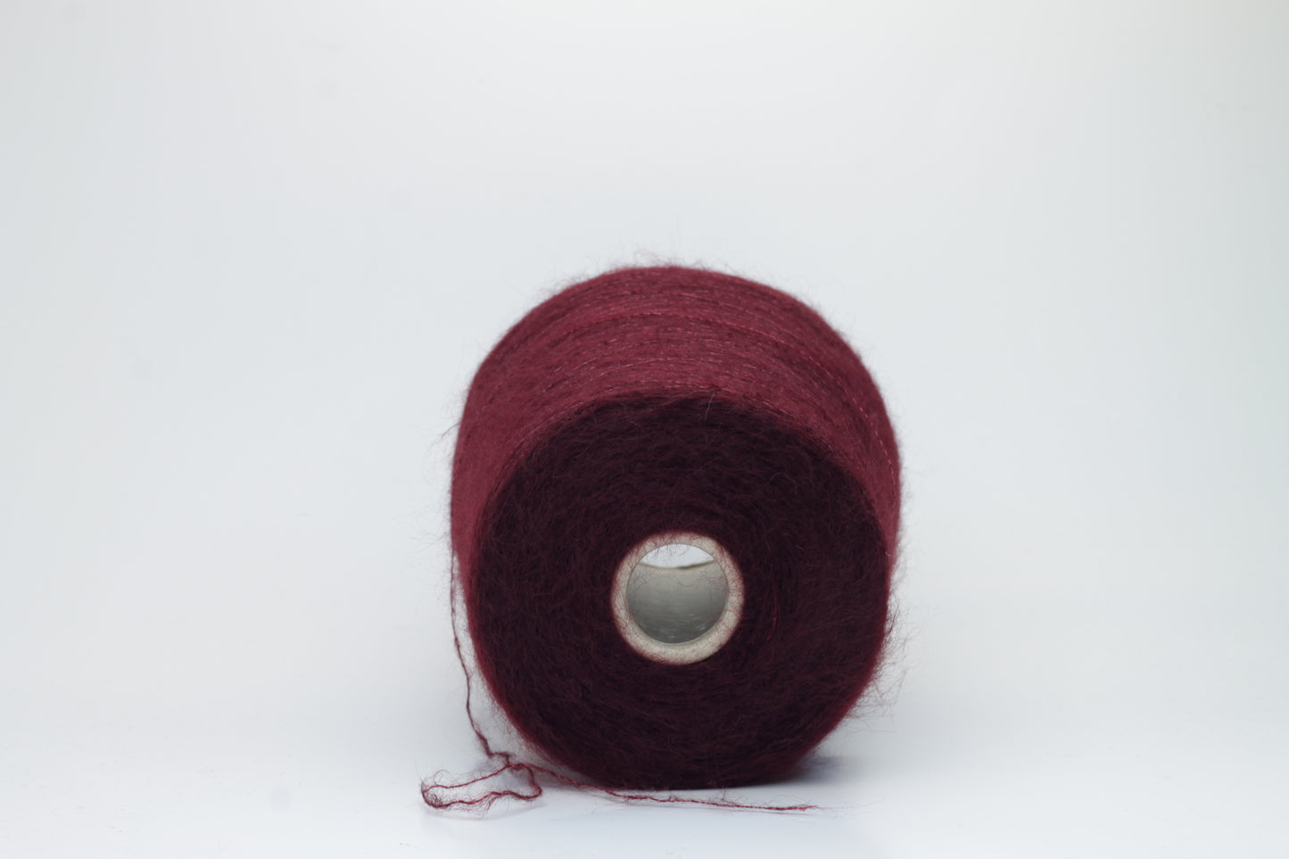 Close-up of fluffy Bordo kid mohair and silk blend yarn, subtly lustrous with a soft halo, gently twisted into a fine, delicate thread.