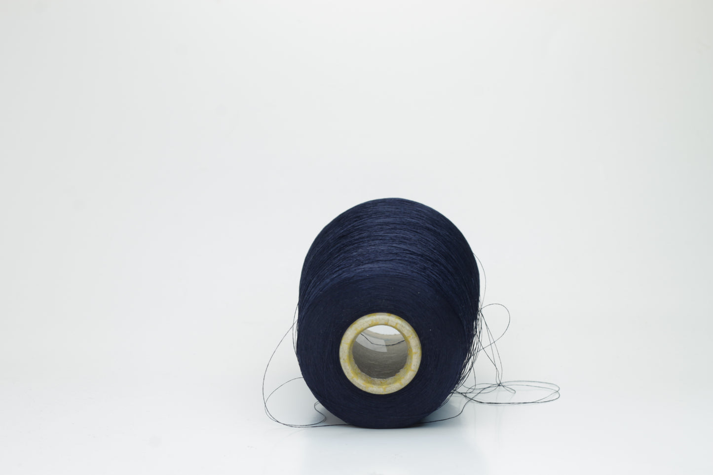 Close-up of a neatly wound spool of fine navy silk yarn, exhibiting a smooth, tightly twisted two-ply structure and a subtle, elegant sheen under direct light. The deep blue color appears rich and consistent.