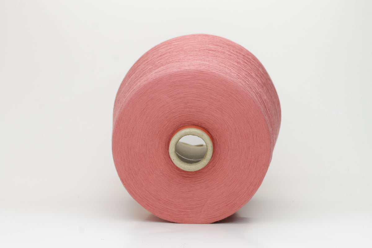 A close-up shows a finely twisted 2-ply strand of soft cotton yarn in a muted dusty rose pink, exhibiting a subtle, even texture and a delicate, gentle sheen.