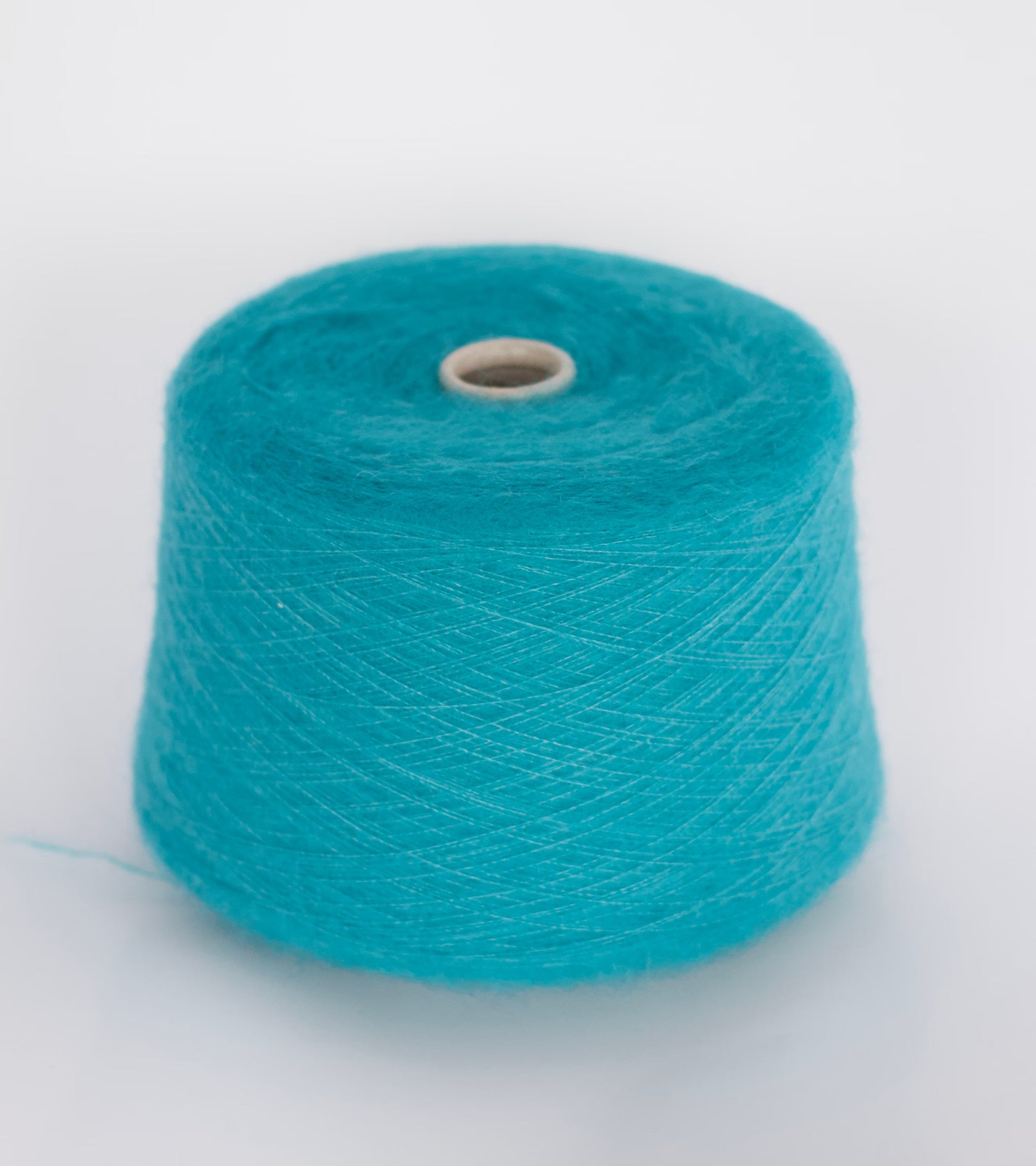 Close-up image showcasing a cone of dark cyan kid mohair yarn, revealing its fluffy texture, subtle sheen, and the complex ply twist of the fibers creating a rich, vibrant color depth.