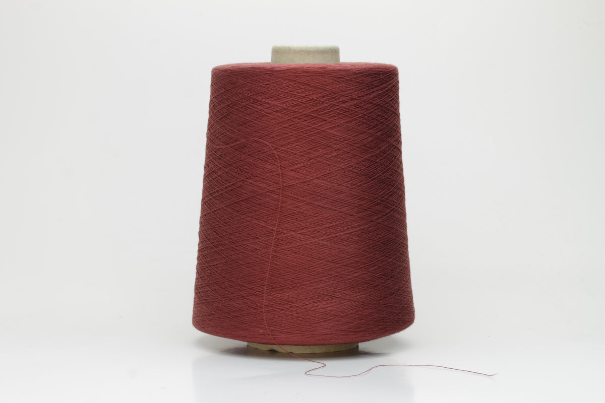 Close-up of a tightly twisted, matte finish cotton yarn in a rich, earthy warm terracotta hue, showcasing its smooth texture and consistent ply structure, ready for crafting.