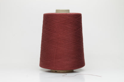 Close-up of a tightly twisted, matte finish cotton yarn in a rich, earthy warm terracotta hue, showcasing its smooth texture and consistent ply structure, ready for crafting.