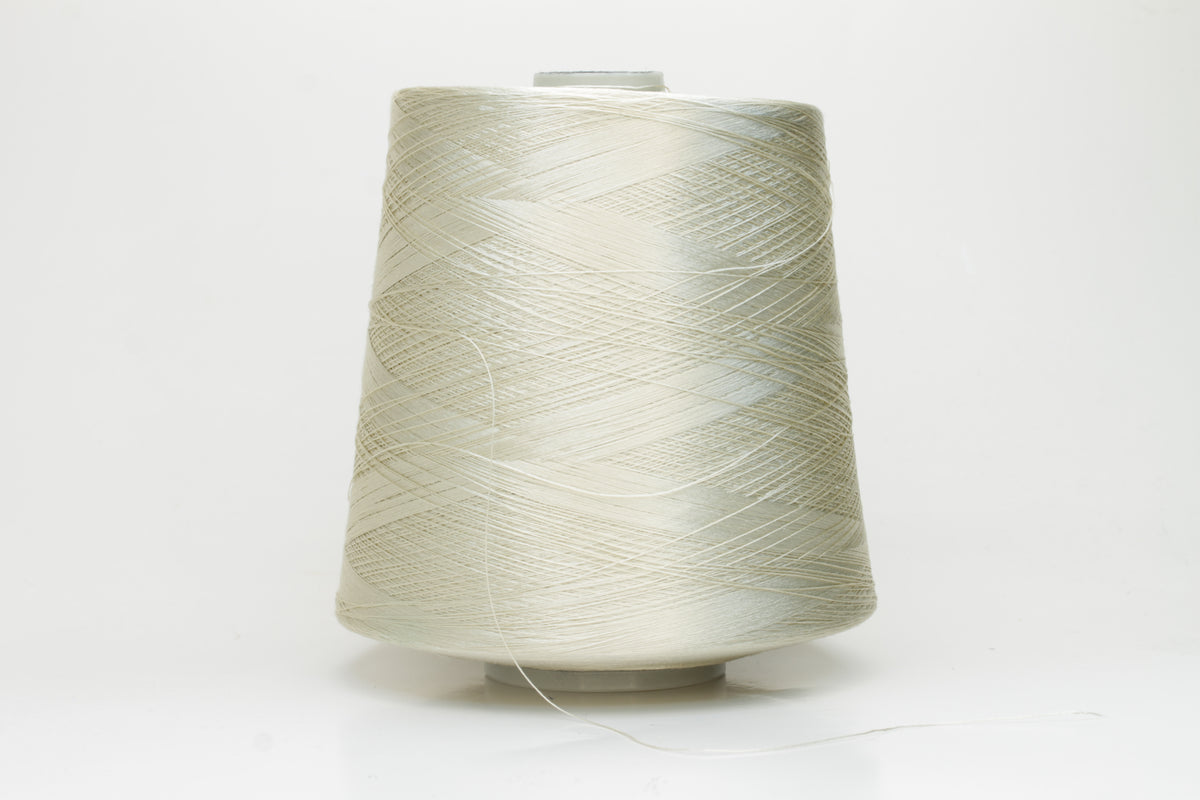 Close-up of finely plied natural silk yarn in a pale, warm champagne tone, reflecting light with a soft, radiant shimmer.