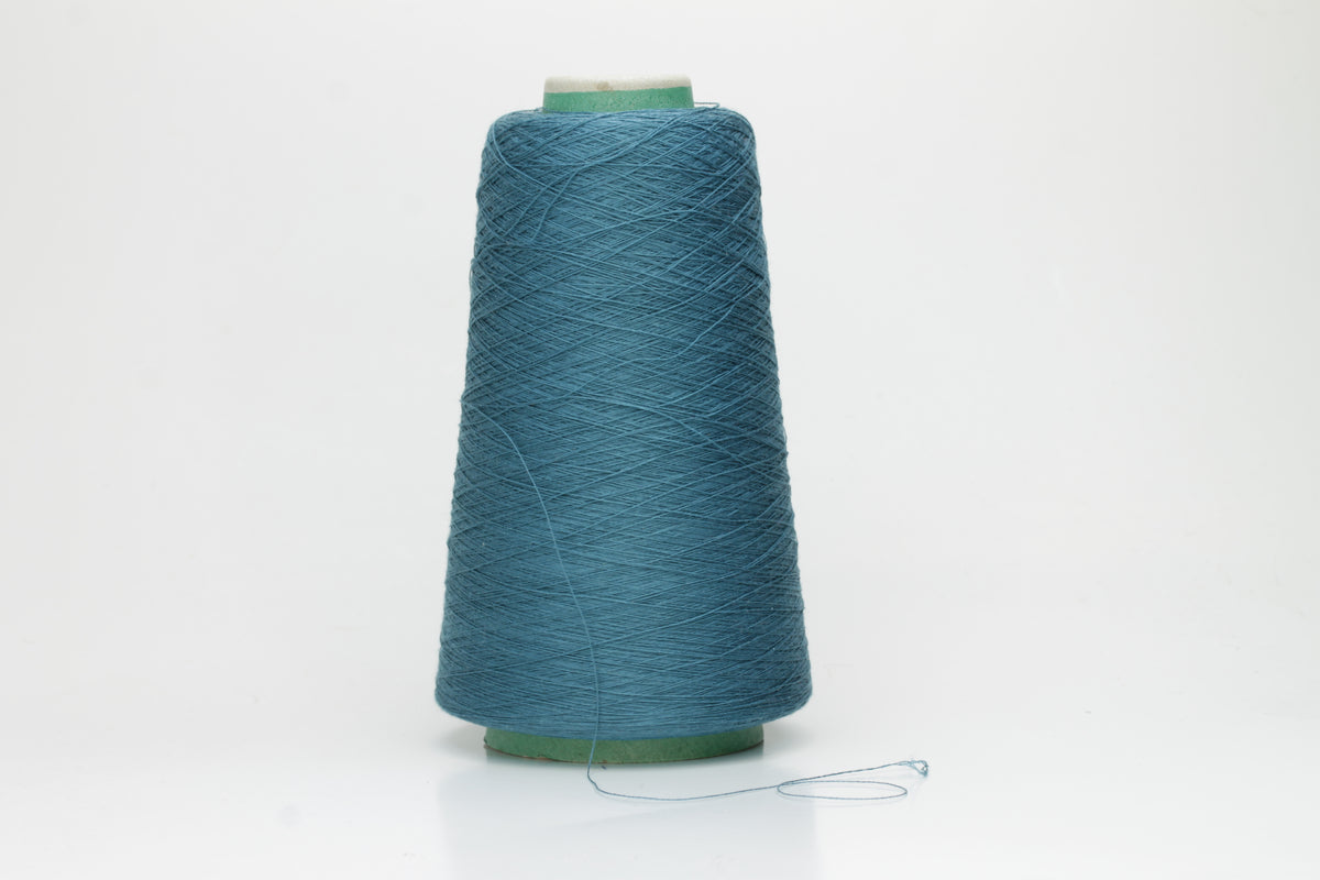 A skein of luxurious 100% pure silk yarn in a deep, shimmering petrol blue, displaying a smooth, finely spun single ply with a high, lustrous sheen.