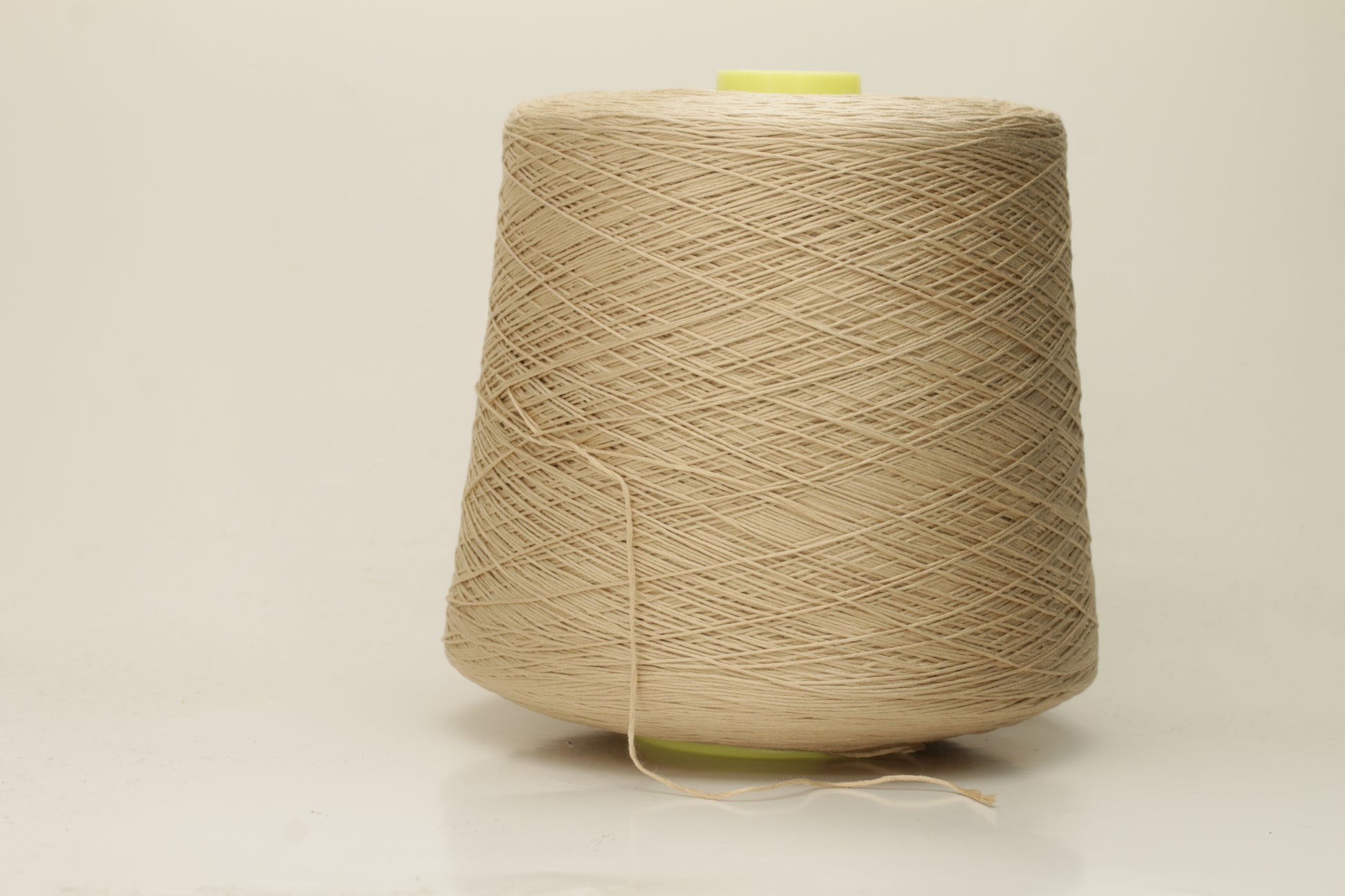 Close-up of a single strand of lustrous, fine-gauge beige silk and cotton yarn, showcasing its smooth, even twist and soft sheen.