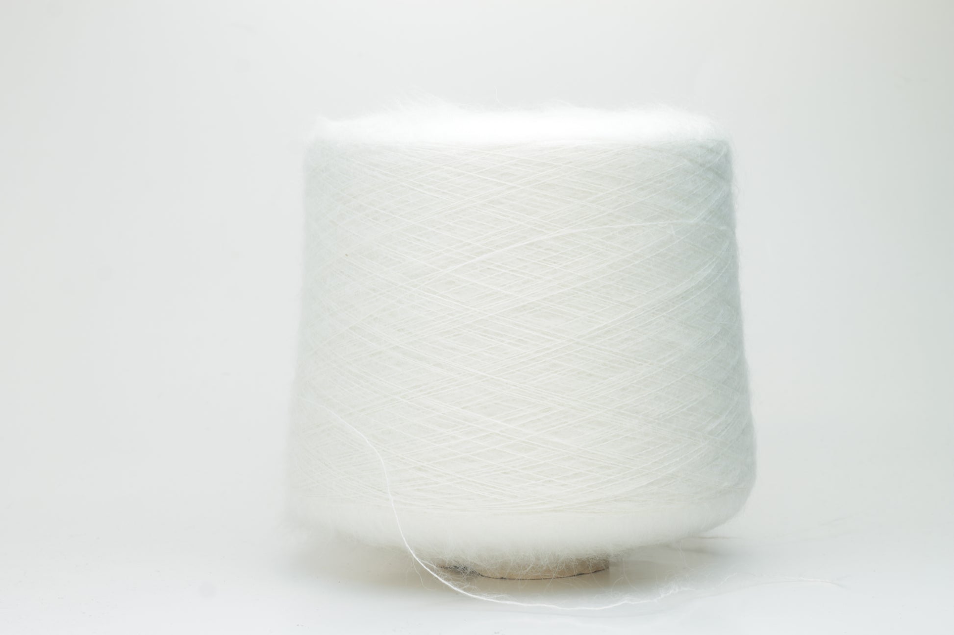 Close-up of fluffy white kid mohair and silk blend yarn, subtly lustrous with a soft halo, gently twisted into a fine, delicate thread.
