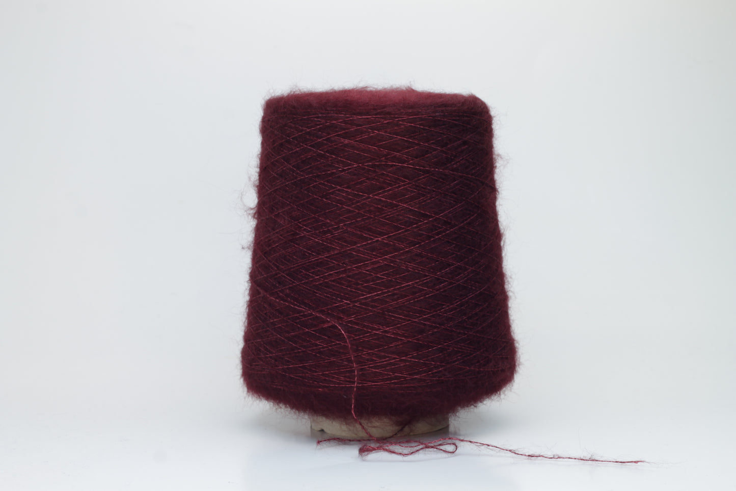 Close-up of fluffy Bordo kid mohair and silk blend yarn, subtly lustrous with a soft halo, gently twisted into a fine, delicate thread.