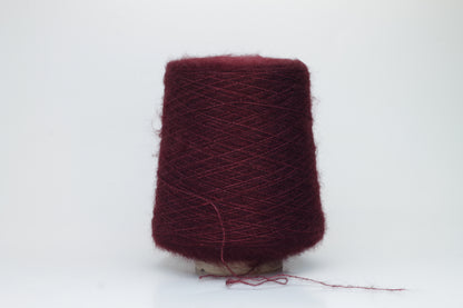 Close-up of fluffy Bordo kid mohair and silk blend yarn, subtly lustrous with a soft halo, gently twisted into a fine, delicate thread.