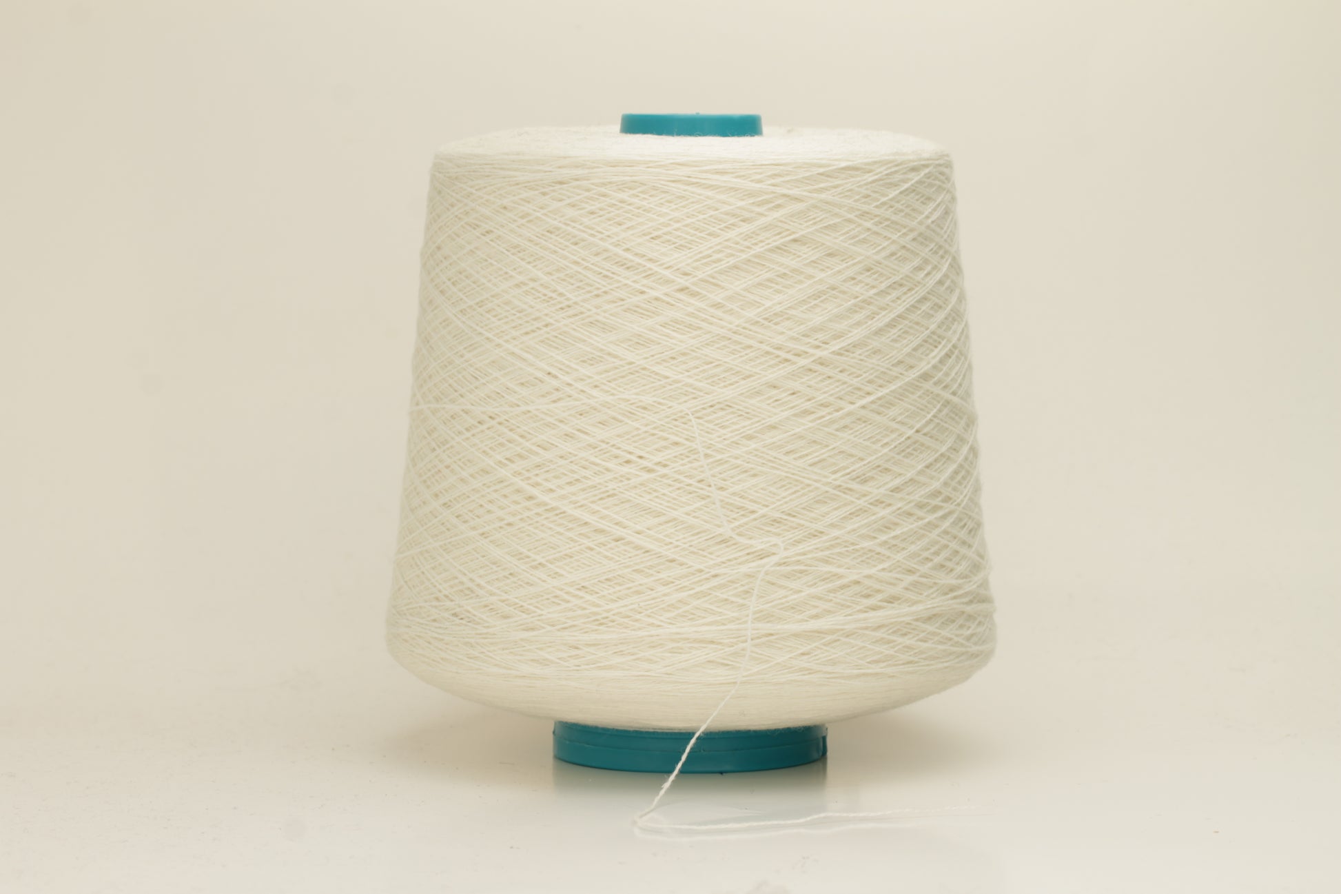 Close-up of a two-ply fine cashmere yarn, tightly twisted with a subtle matte sheen in a creamy off-white Gesso color.