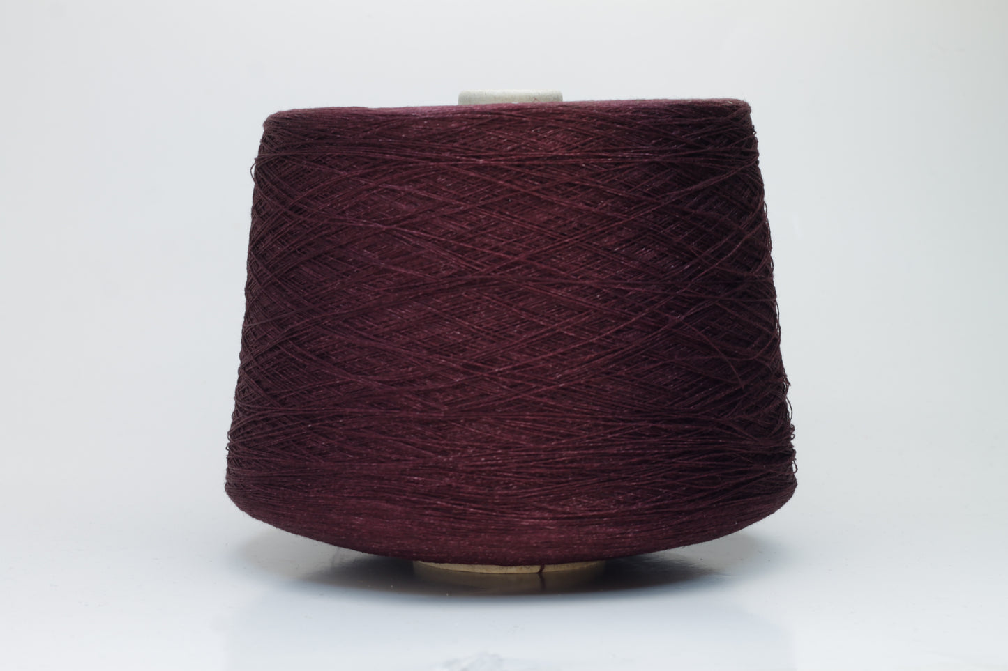 Close-up of a neatly wound cone of deep wine-red 2-ply linen yarn, exhibiting a subtle natural sheen and distinct crisp texture.