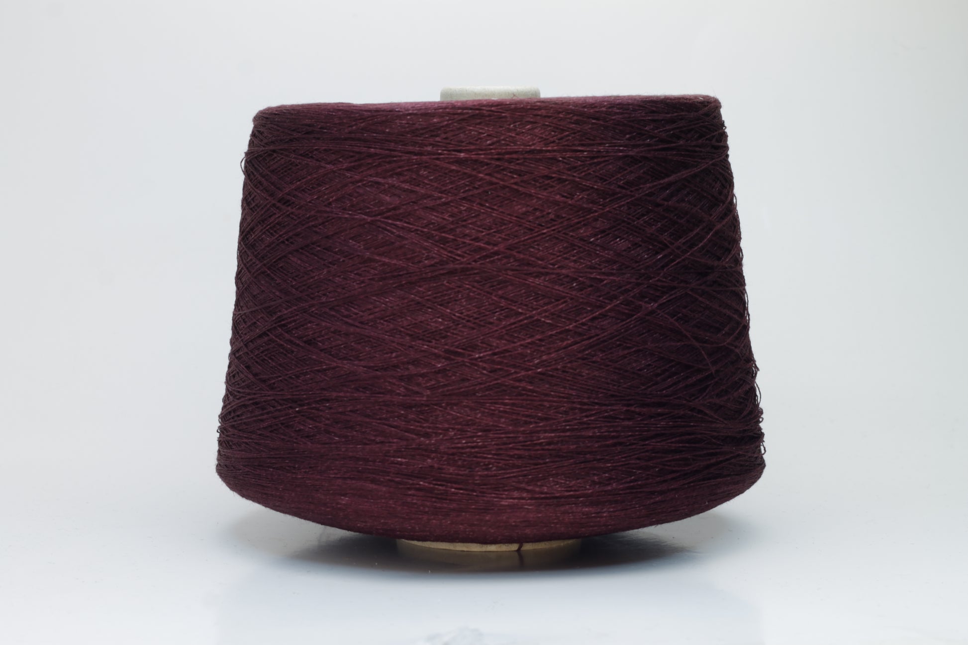 Close-up of a neatly wound cone of deep wine-red 2-ply linen yarn, exhibiting a subtle natural sheen and distinct crisp texture.