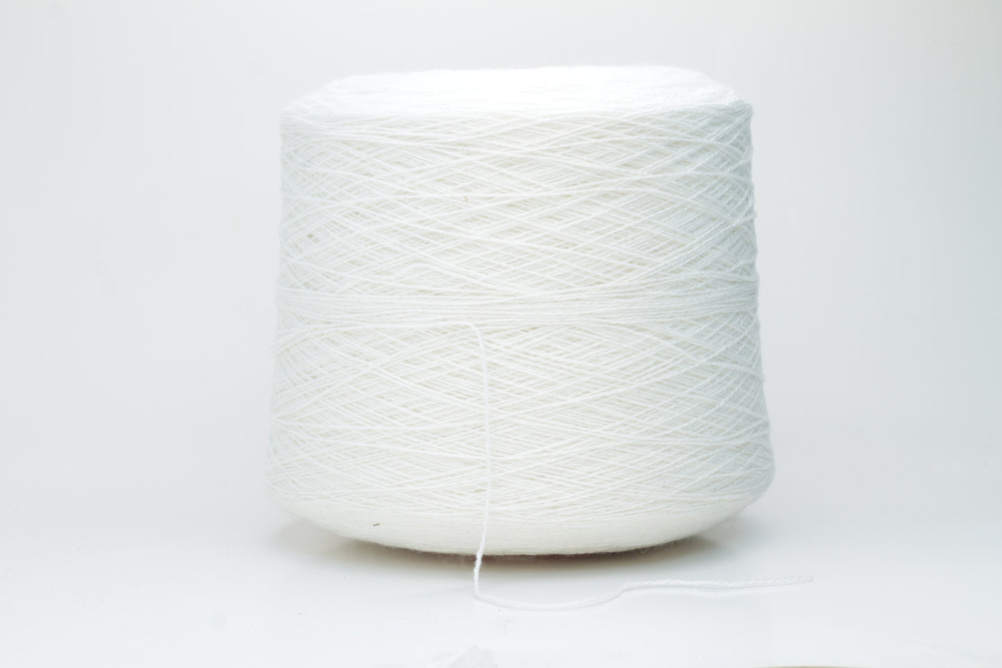 Close-up of pristine white, finely plied 100% cashmere yarn, showcasing its soft halo and subtle sheen on a neutral background.
