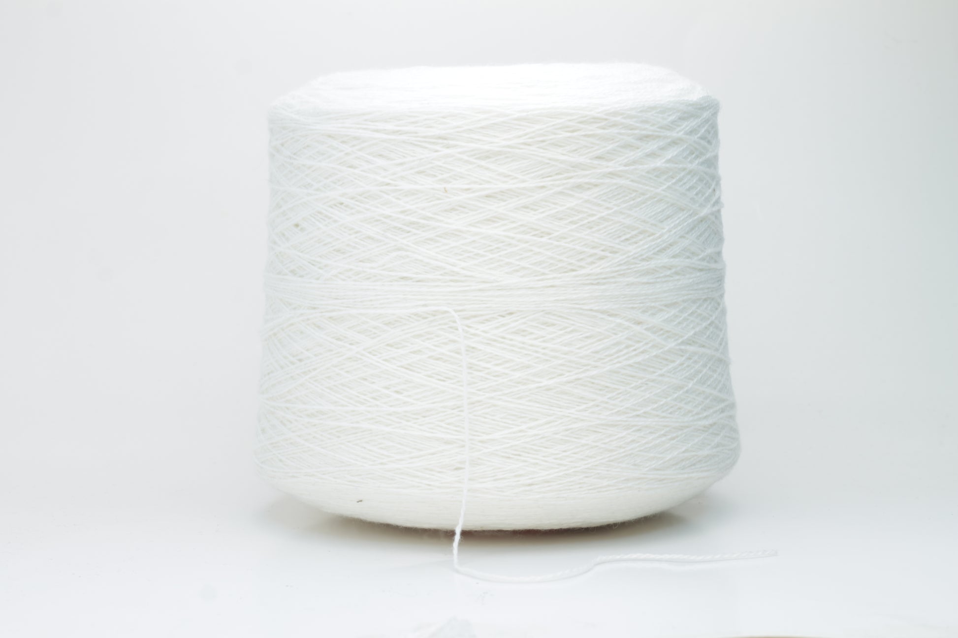 Close-up of pristine white, finely plied 100% cashmere yarn, showcasing its soft halo and subtle sheen on a neutral background.