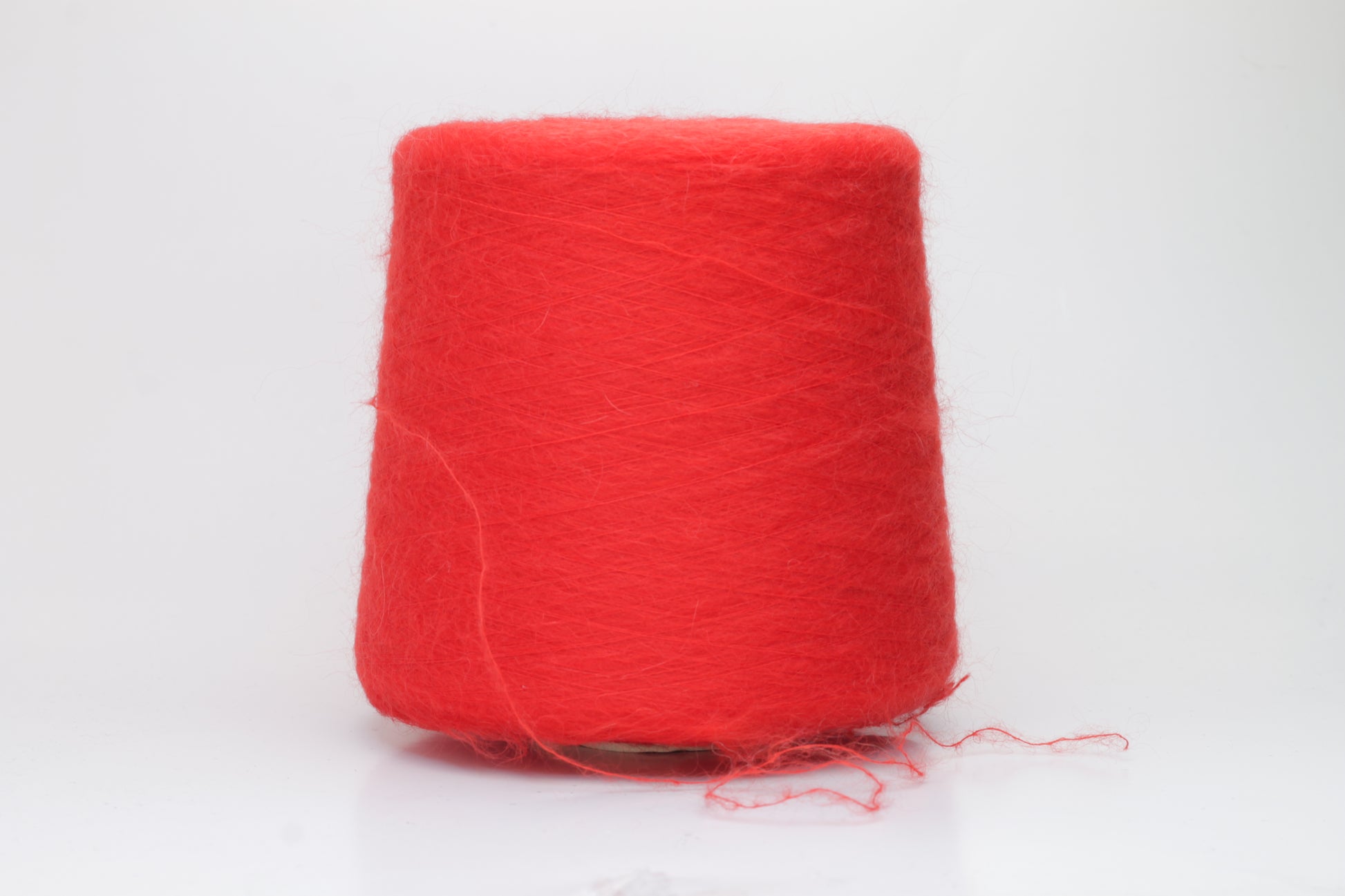 Close-up view of vibrant red SuperKidMohair yarn featuring a dense, fluffy pile with subtle sheen. The ply twist is evident in the slightly twisted structure, creating a soft and luxurious tactile experience.