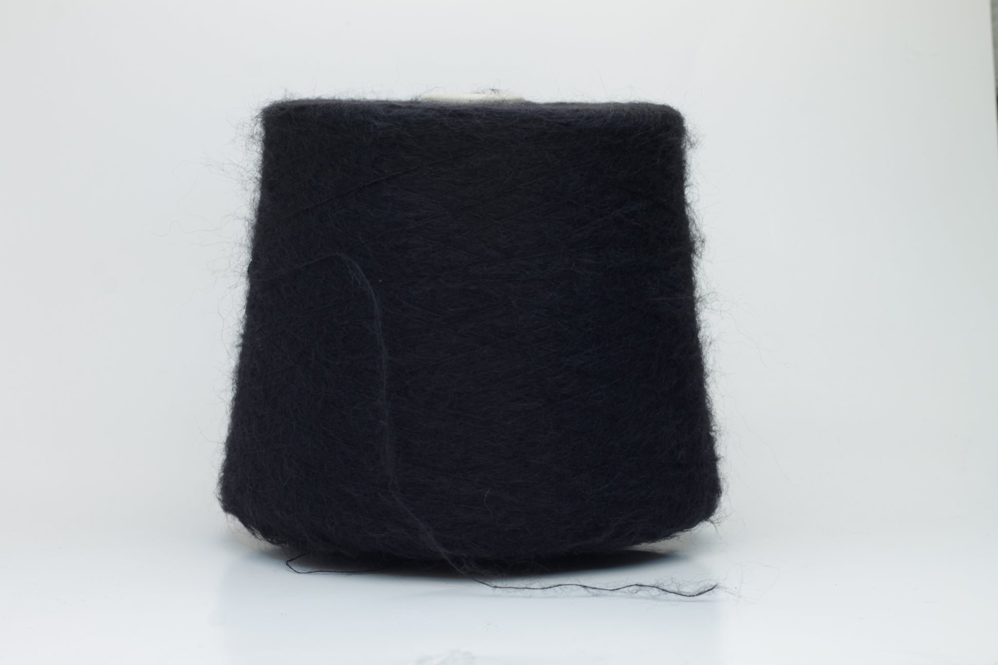 Close-up shot of the Black SuperKidMohair yarn, showcasing its dense ply twist and subtle sheen. The fibers appear fluffy and richly colored, creating a luxurious tactile impression.