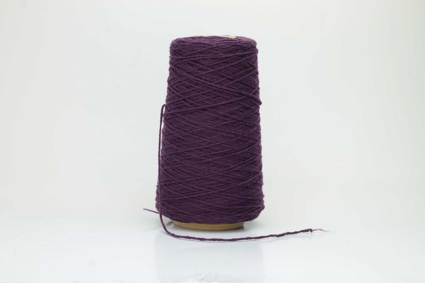A soft, single-ply cashmere yarn in a deep, rich purple hue, gently coiled, displaying a delicate halo of fluffiness and a subtle, luxurious sheen.