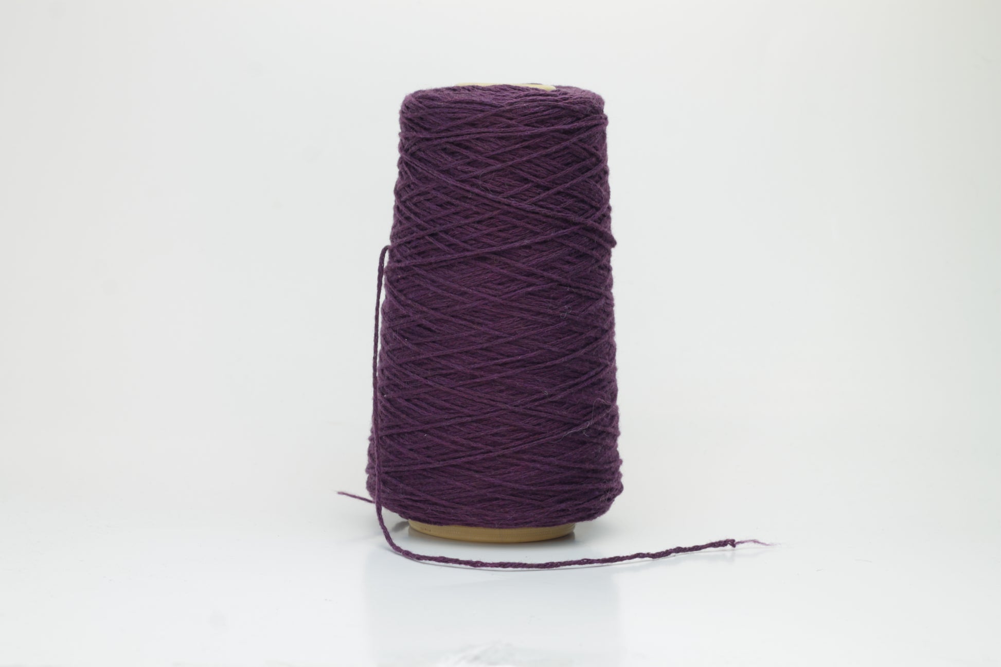 A soft, single-ply cashmere yarn in a deep, rich purple hue, gently coiled, displaying a delicate halo of fluffiness and a subtle, luxurious sheen.