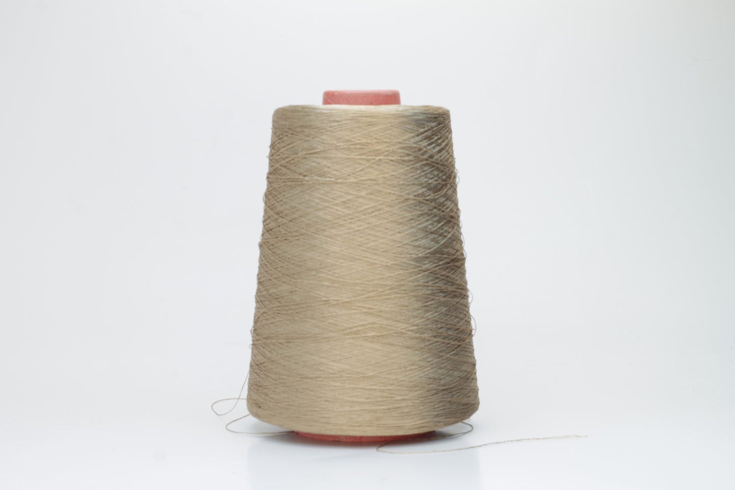 Finely spun single-ply natural beige silk yarn, smoothly wound into a compact cake, exhibiting a high, natural sheen. The thread has a crisp, uniform structure with no visible fluffiness.