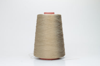 Finely spun single-ply natural beige silk yarn, smoothly wound into a compact cake, exhibiting a high, natural sheen. The thread has a crisp, uniform structure with no visible fluffiness.