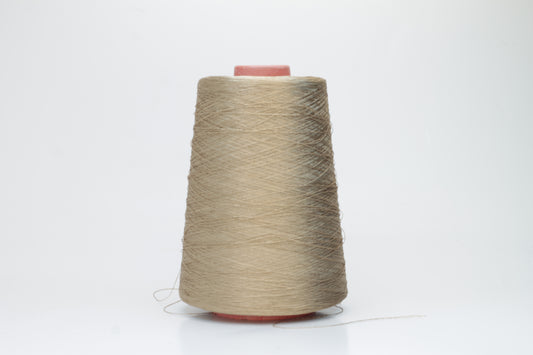 Finely spun single-ply natural beige silk yarn, smoothly wound into a compact cake, exhibiting a high, natural sheen. The thread has a crisp, uniform structure with no visible fluffiness.