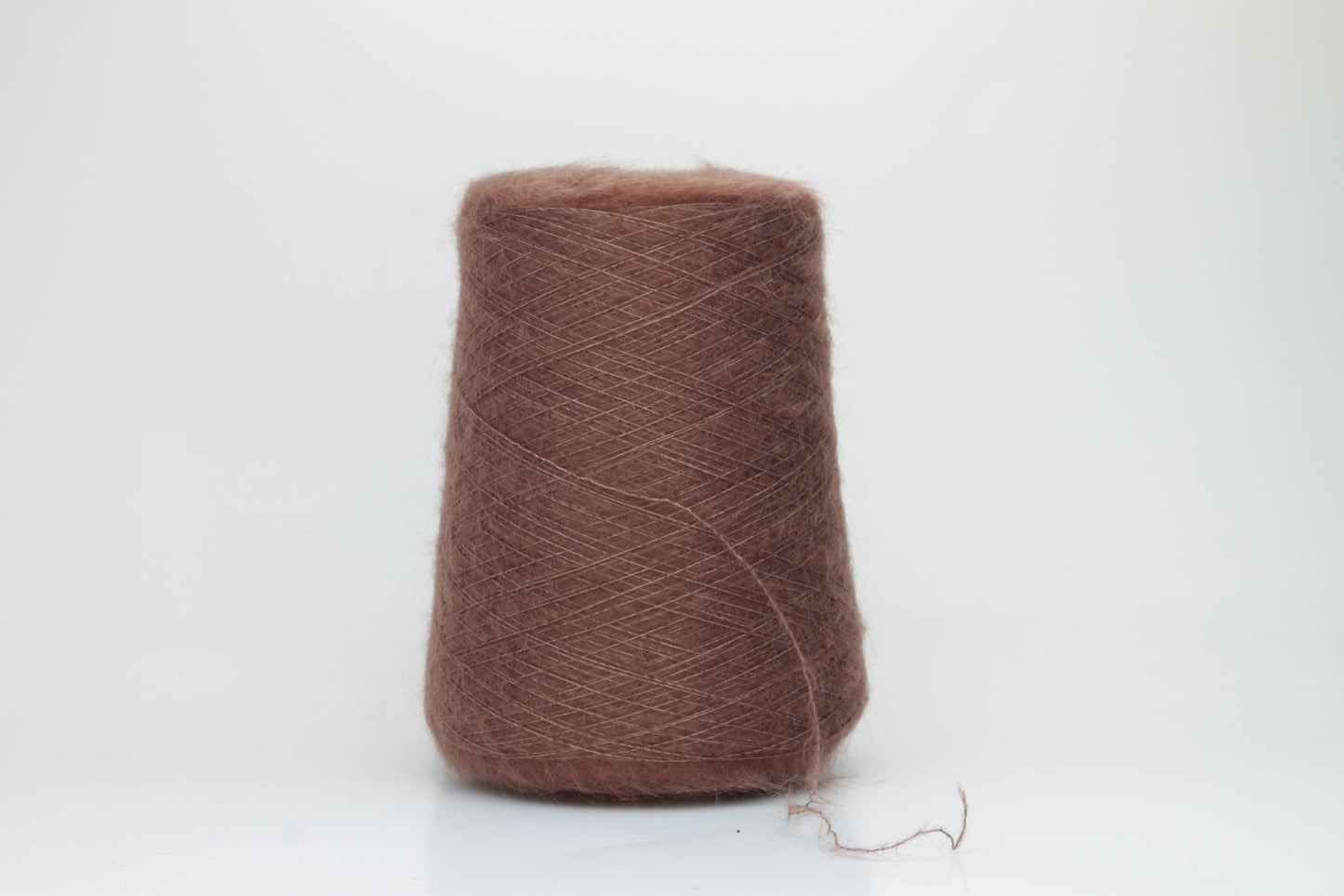 Close-up of fluffy Marrone kid mohair and silk blend yarn, subtly lustrous with a soft halo, gently twisted into a fine, delicate thread.
