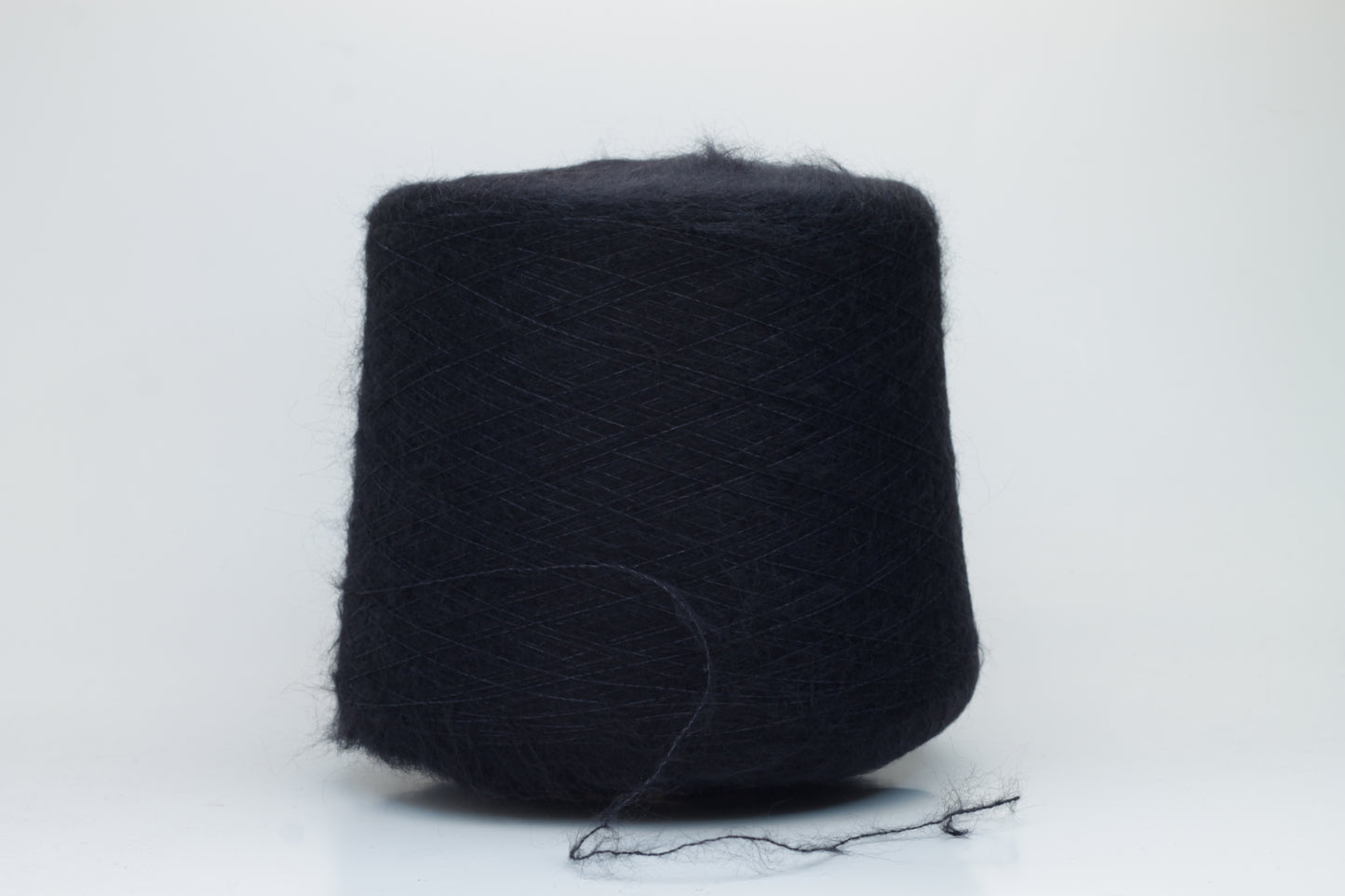 Close-up of fluffy Black kid mohair and silk blend yarn, subtly lustrous with a soft halo, gently twisted into a fine, delicate thread.