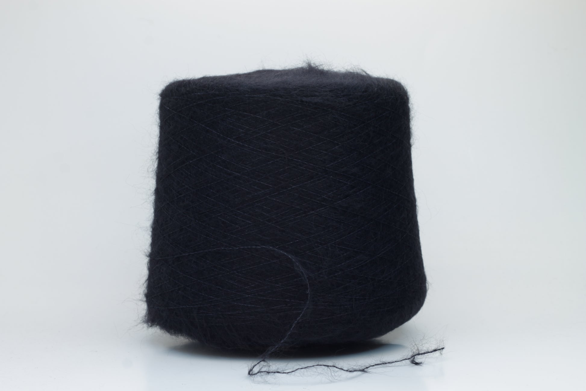 Close-up of fluffy Black kid mohair and silk blend yarn, subtly lustrous with a soft halo, gently twisted into a fine, delicate thread.