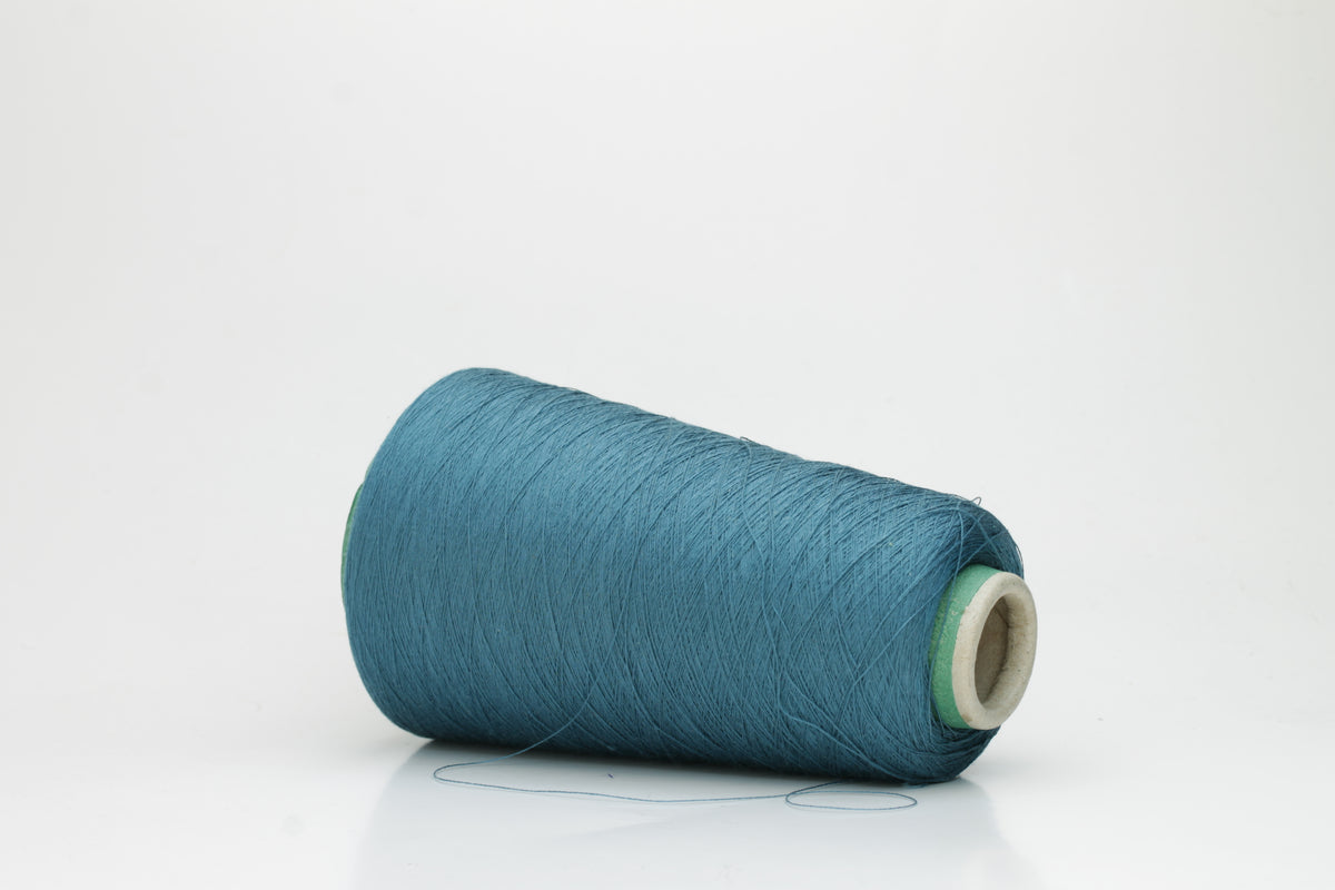 A skein of luxurious 100% pure silk yarn in a deep, shimmering petrol blue, displaying a smooth, finely spun single ply with a high, lustrous sheen.