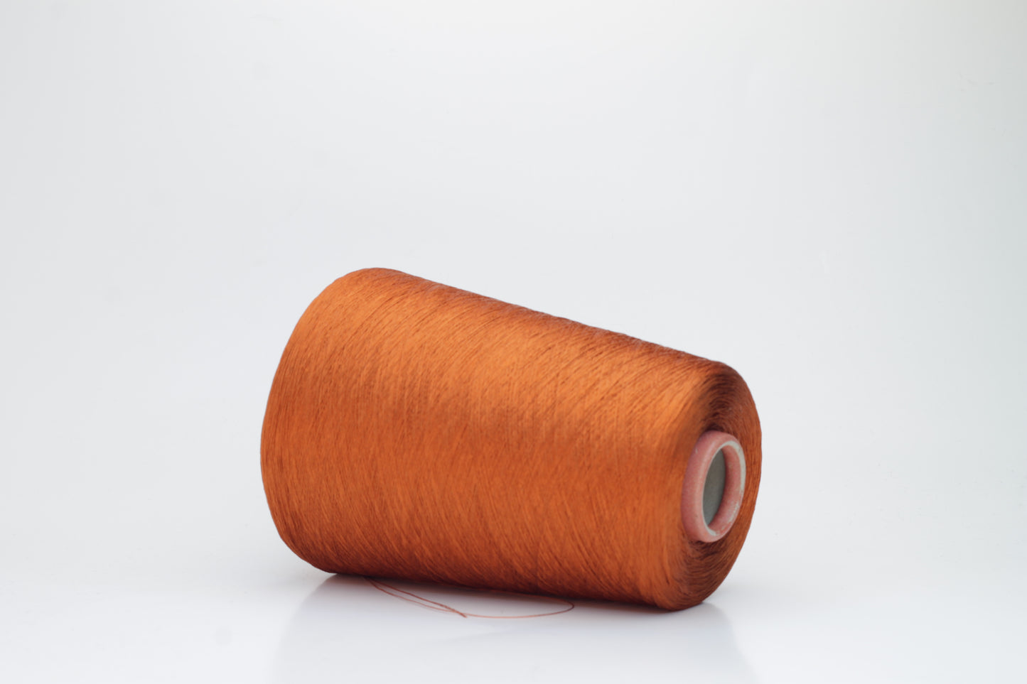 Close-up of a meticulously spun, single-ply bright orange silk yarn with a crisp, almost translucent quality and brilliant sheen.