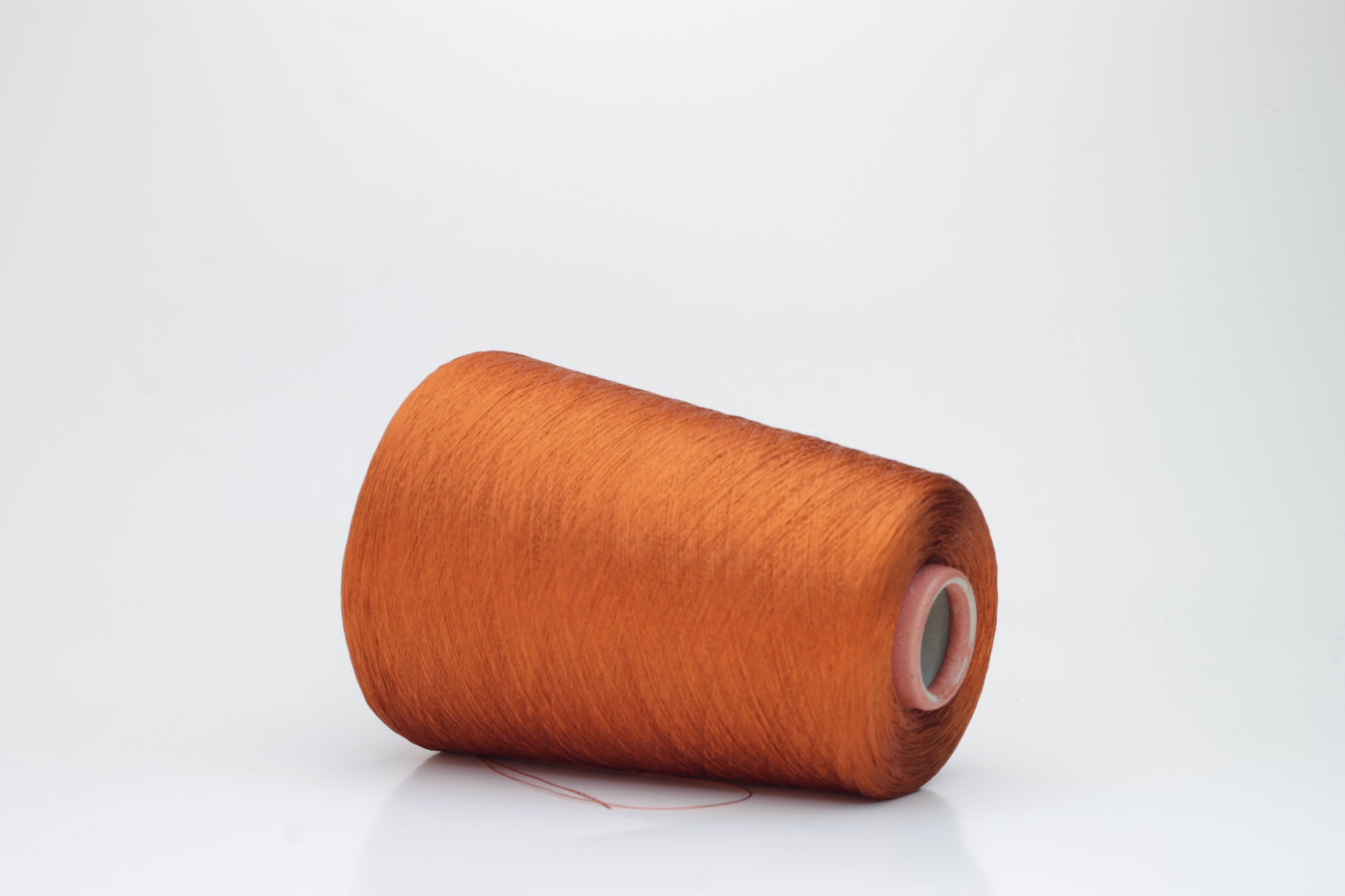 Close-up of a meticulously spun, single-ply bright orange silk yarn with a crisp, almost translucent quality and brilliant sheen.