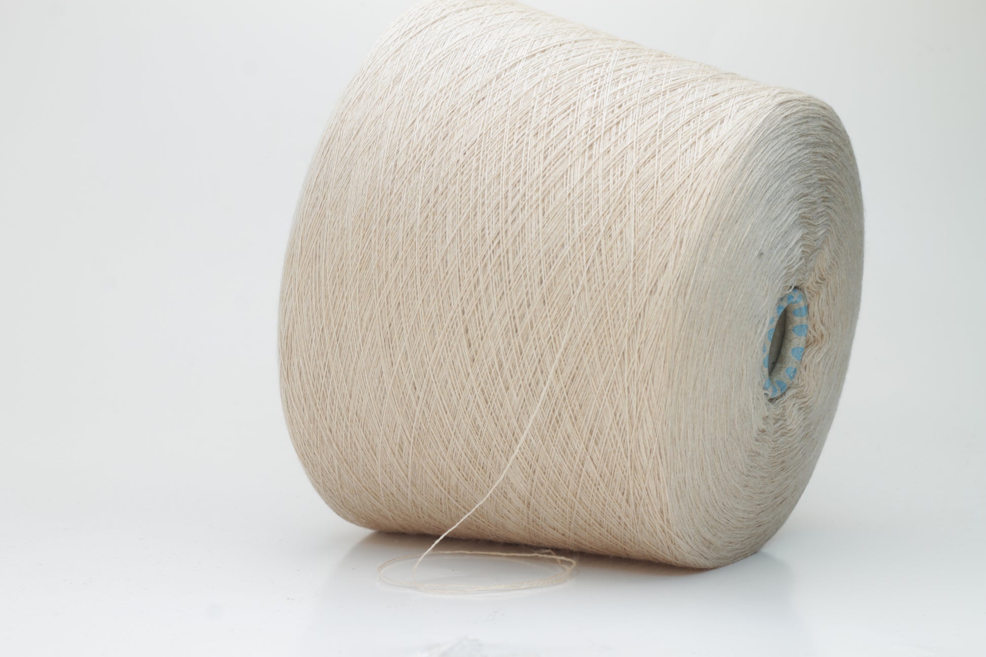 Close-up shot of creamy beige merino yarn, featuring a tight ply twist and a subtle sheen. The fibers exhibit exceptional fluffiness and texture, ideal for intricate knitting patterns.