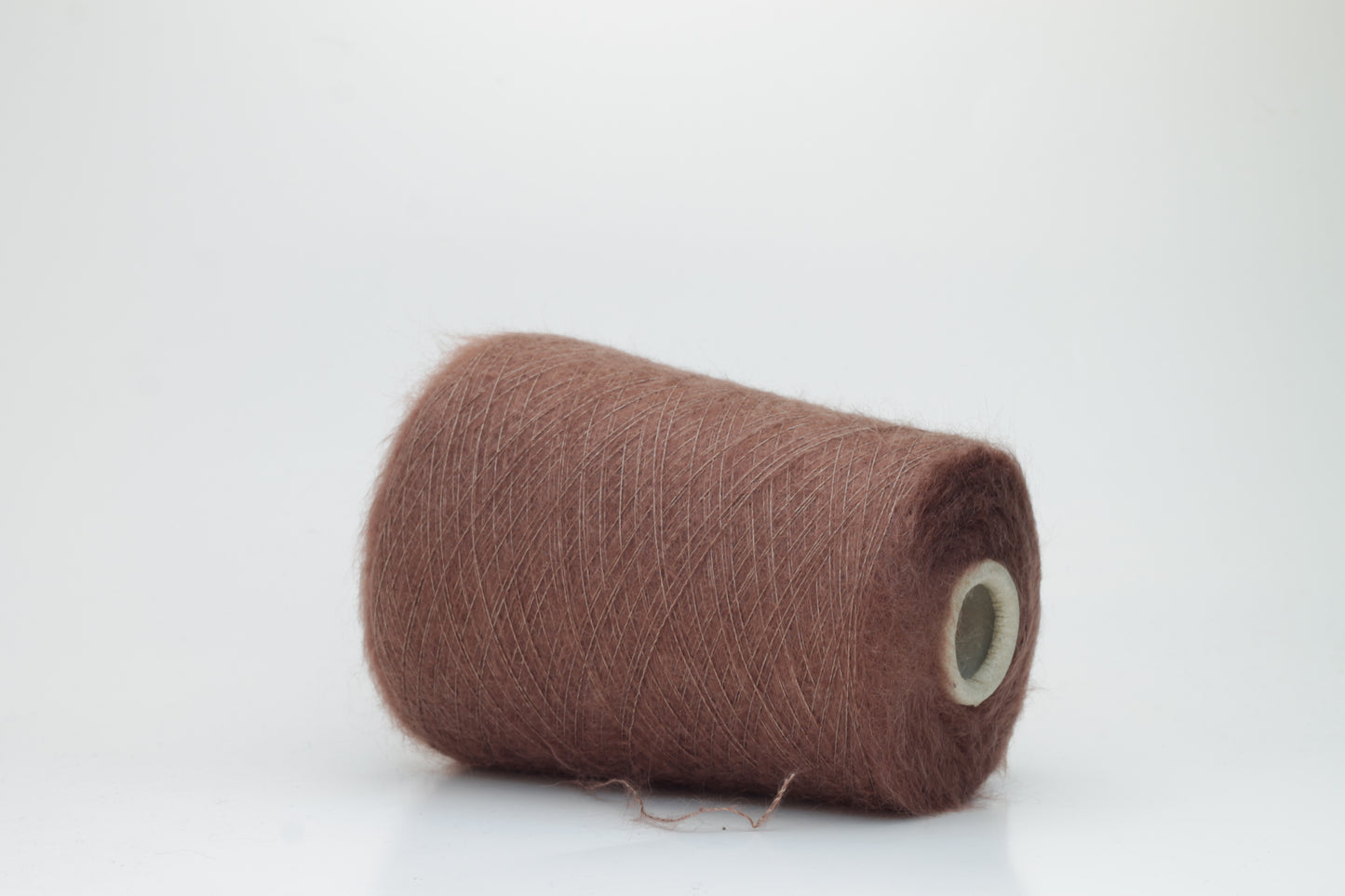 Close-up of fluffy Marrone kid mohair and silk blend yarn, subtly lustrous with a soft halo, gently twisted into a fine, delicate thread.