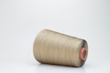 Finely spun single-ply natural beige silk yarn, smoothly wound into a compact cake, exhibiting a high, natural sheen. The thread has a crisp, uniform structure with no visible fluffiness.