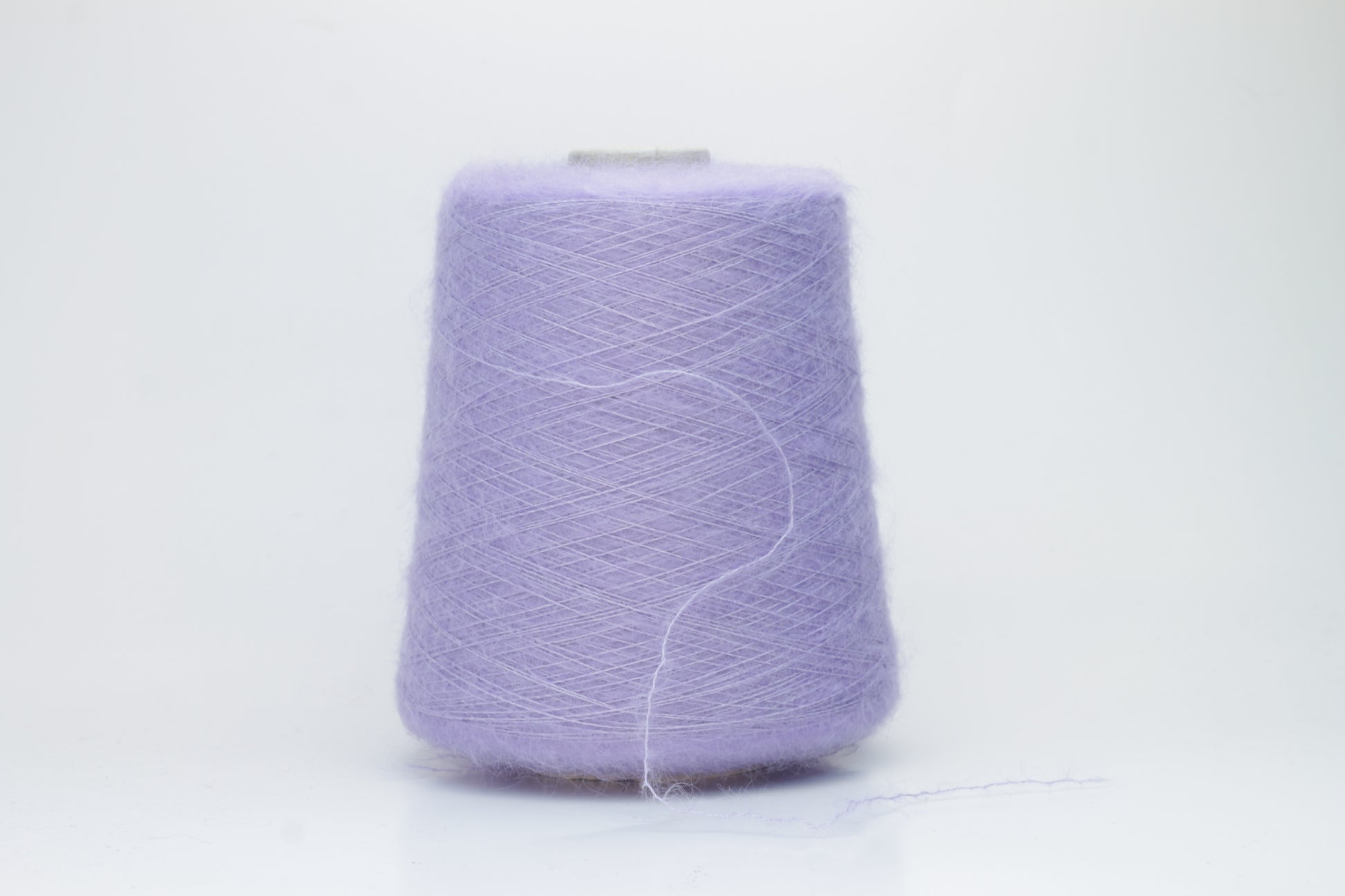 Close-up of fluffy Lila kid mohair and silk blend yarn, subtly lustrous with a soft halo, gently twisted into a fine, delicate thread.