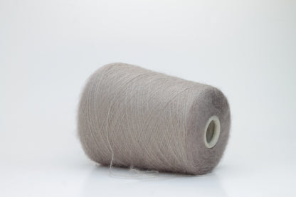 Close-up of fluffy Beige kid mohair and silk blend yarn, subtly lustrous with a soft halo, gently twisted into a fine, delicate thread.
