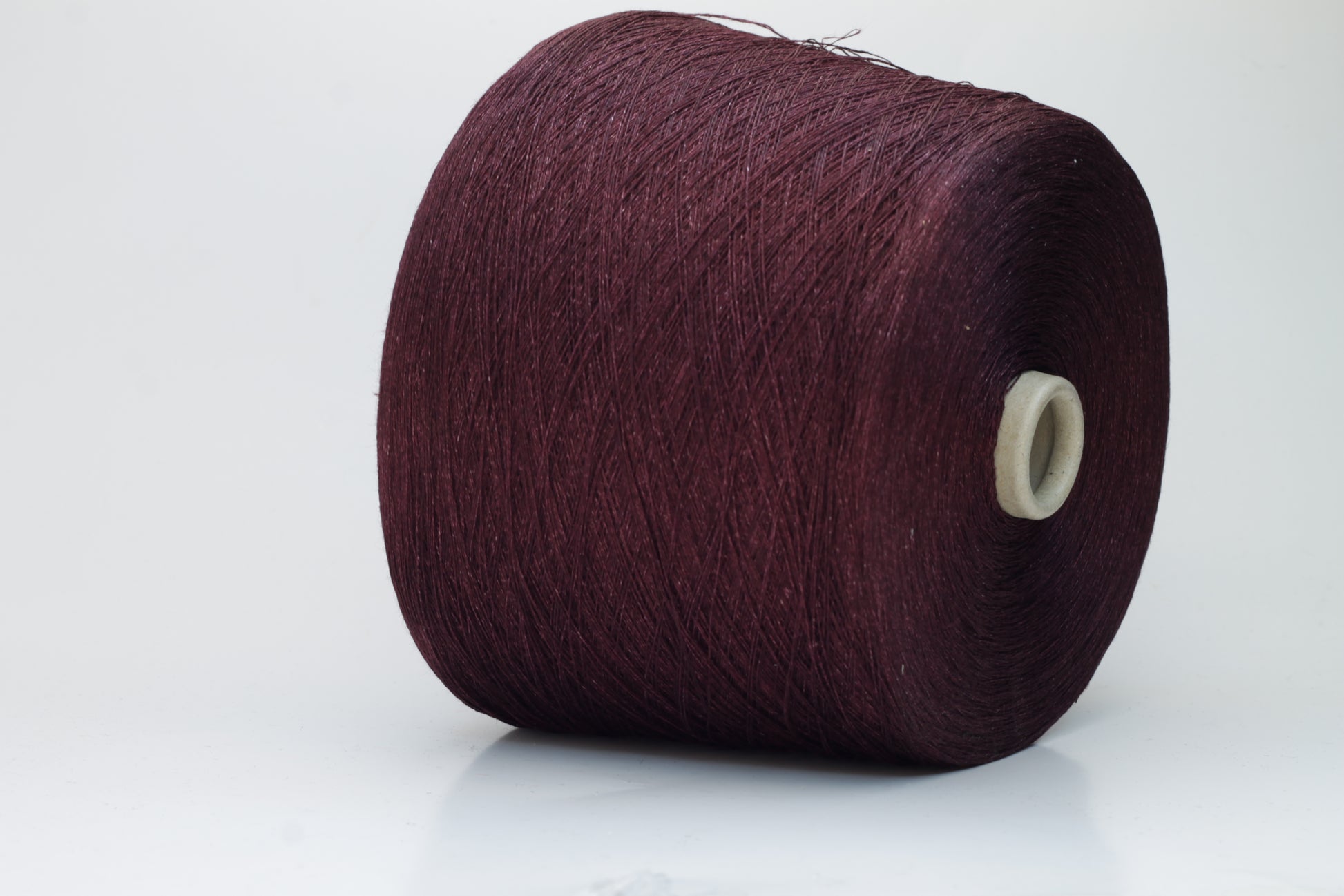 Close-up of a neatly wound cone of deep wine-red 2-ply linen yarn, exhibiting a subtle natural sheen and distinct crisp texture.