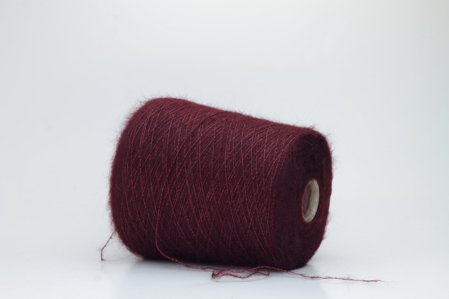 Close-up of fluffy Bordo kid mohair and silk blend yarn, subtly lustrous with a soft halo, gently twisted into a fine, delicate thread.