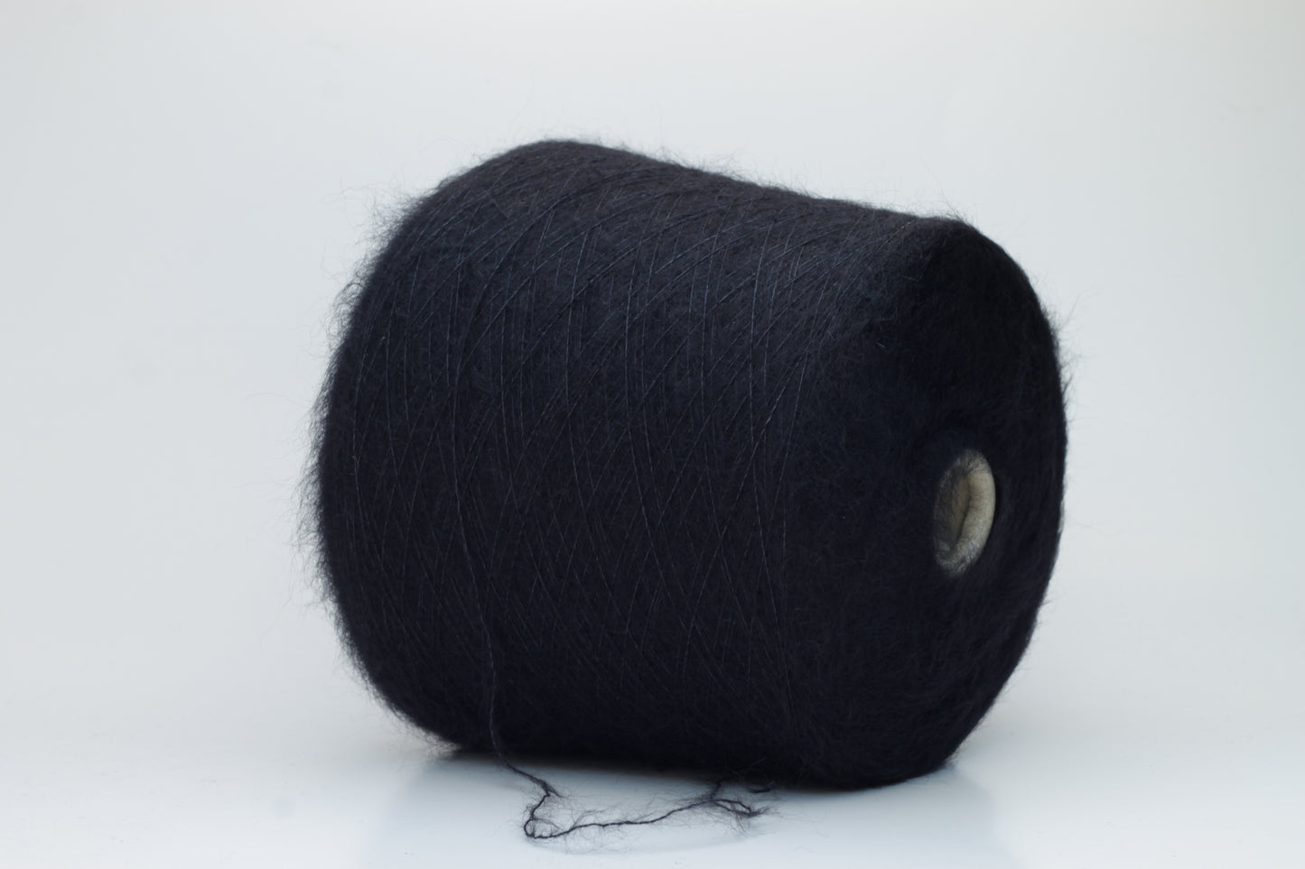 Close-up of fluffy Black kid mohair and silk blend yarn, subtly lustrous with a soft halo, gently twisted into a fine, delicate thread.