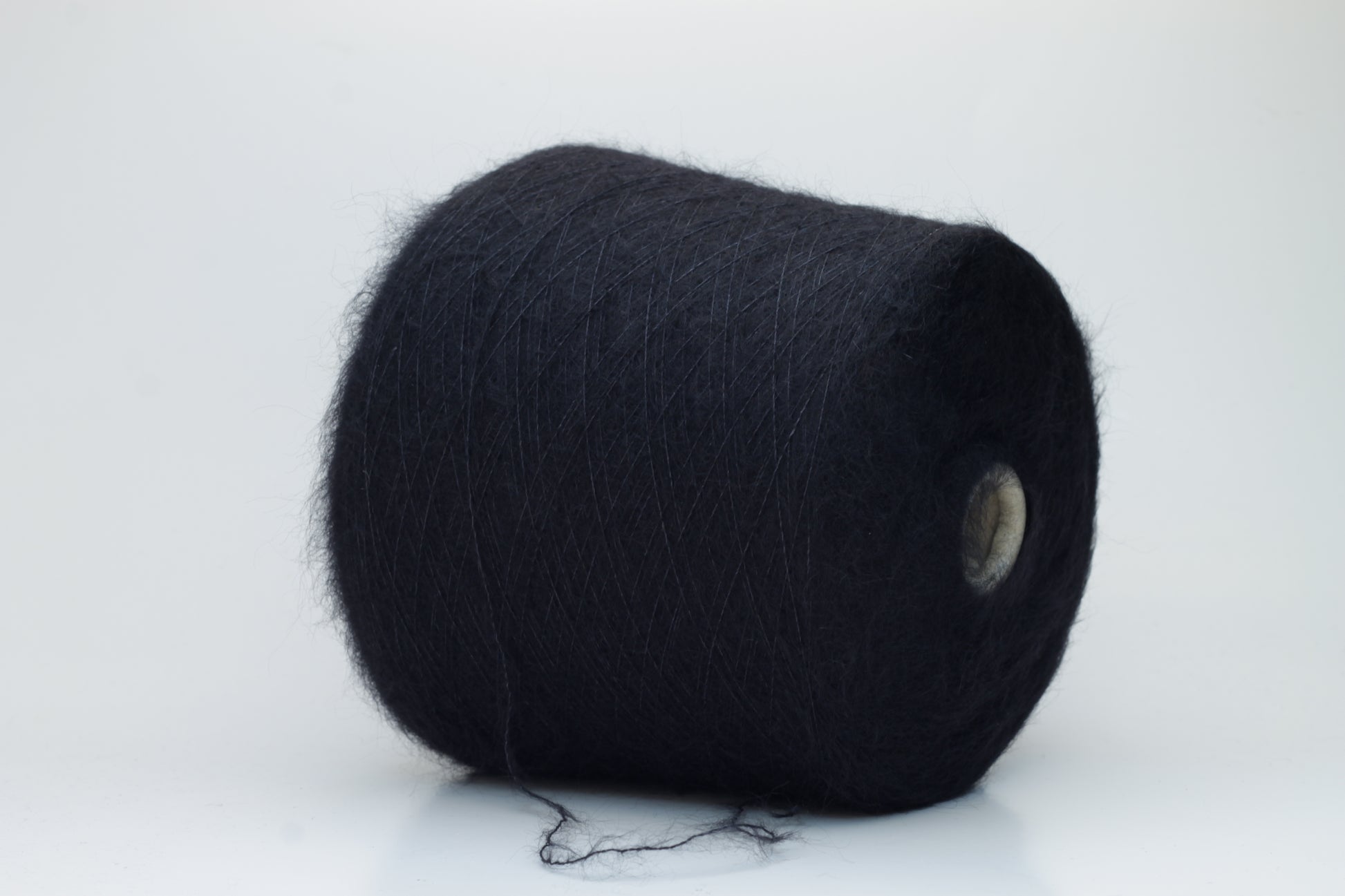 Close-up of fluffy Black kid mohair and silk blend yarn, subtly lustrous with a soft halo, gently twisted into a fine, delicate thread.