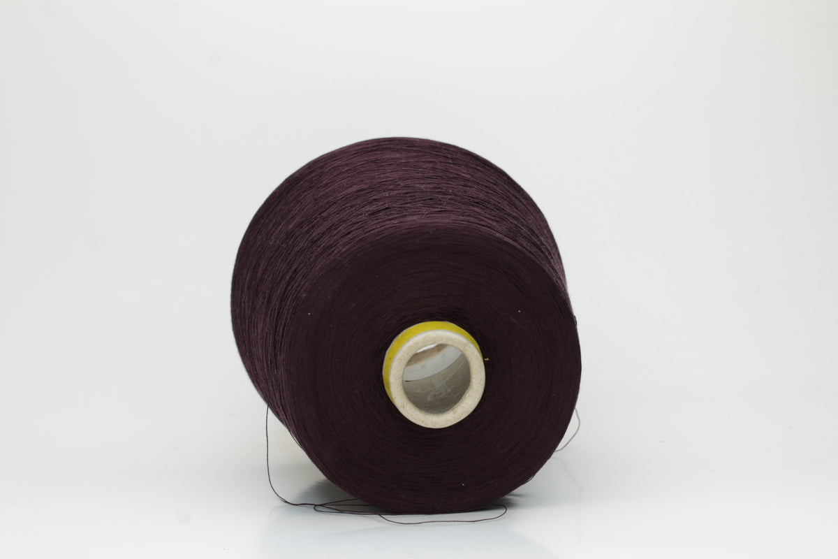 Close-up of a tightly wound cone of smooth, fine cotton yarn in a rich, deep eggplant color, showing a subtle sheen and even 3-ply twist.