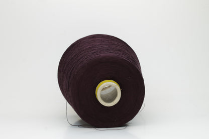 Close-up of a tightly wound cone of smooth, fine cotton yarn in a rich, deep eggplant color, showing a subtle sheen and even 3-ply twist.