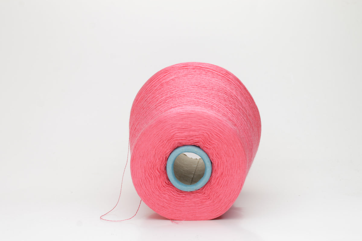 Close-up of a single ply, highly lustrous, smooth bright coral pink silk yarn with a subtle, delicate twist. The color is deep and vibrant.