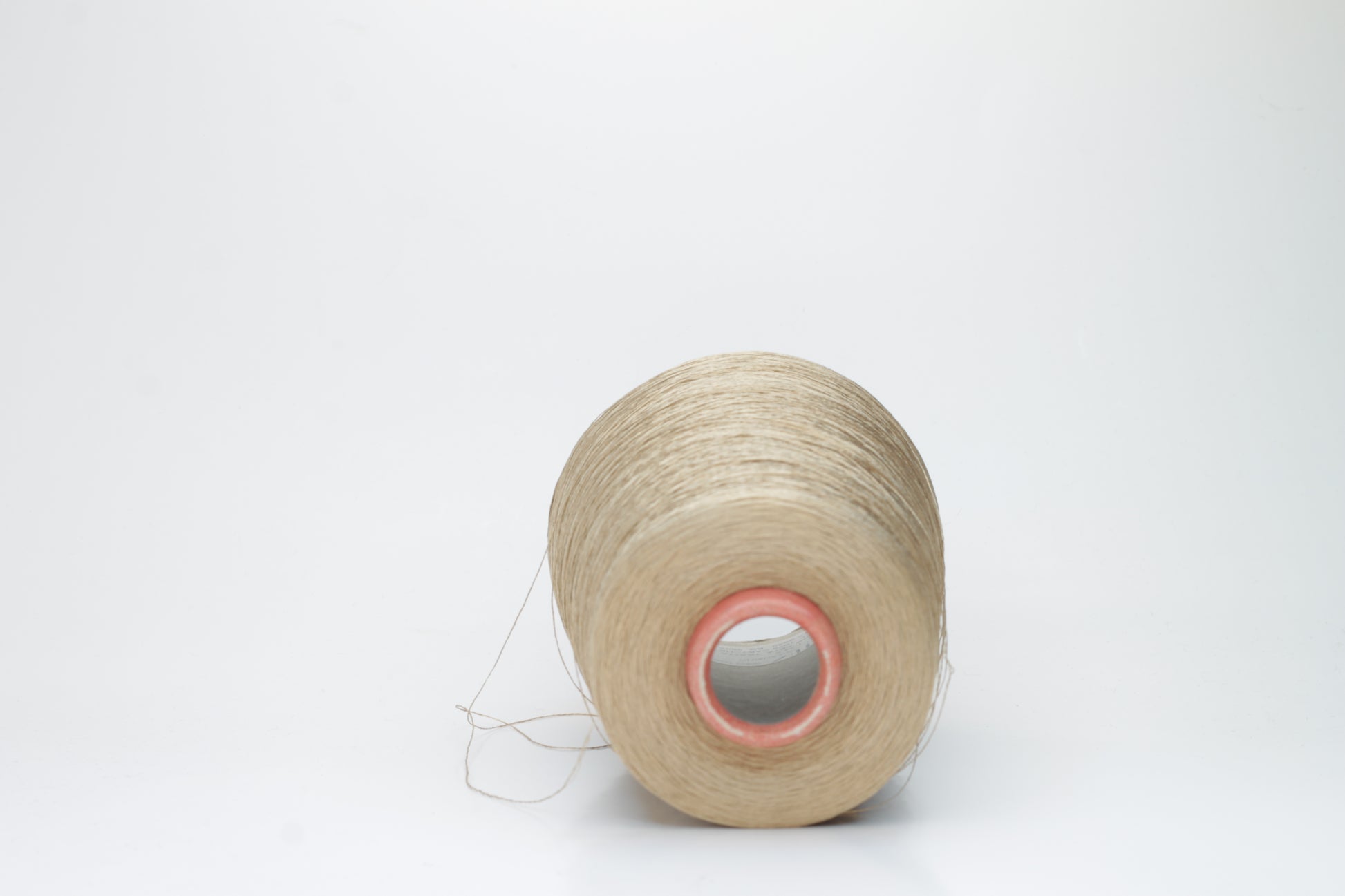 Finely spun single-ply natural beige silk yarn, smoothly wound into a compact cake, exhibiting a high, natural sheen. The thread has a crisp, uniform structure with no visible fluffiness.