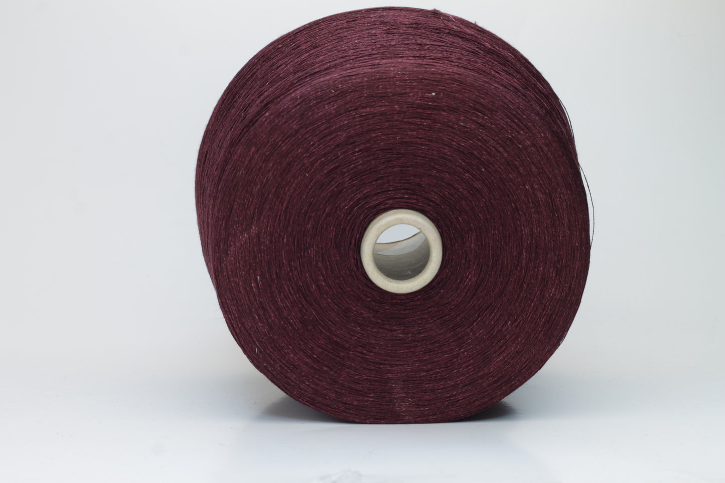 Close-up of a neatly wound cone of deep wine-red 2-ply linen yarn, exhibiting a subtle natural sheen and distinct crisp texture.