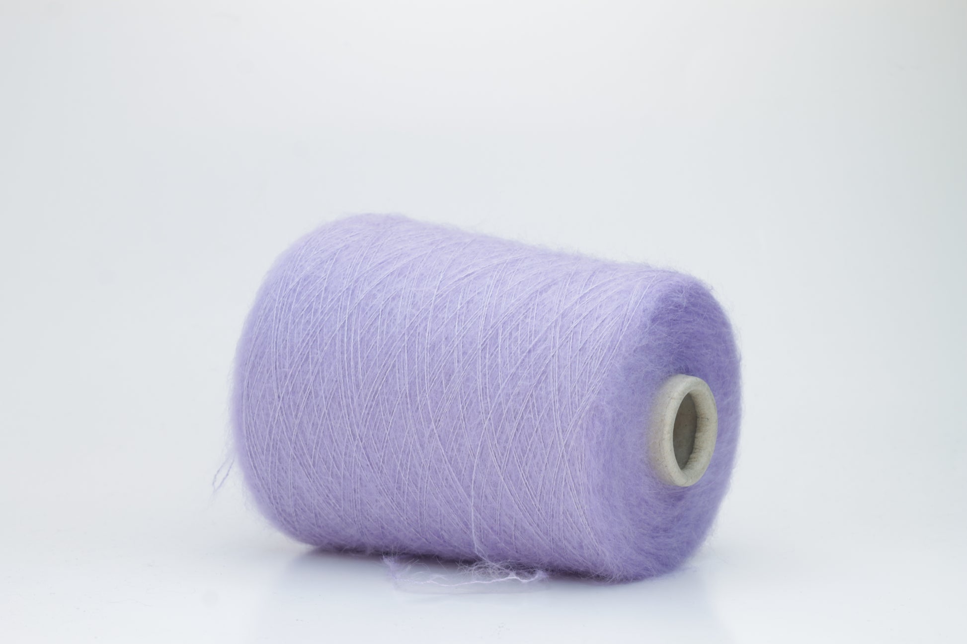 Close-up of fluffy Lila kid mohair and silk blend yarn, subtly lustrous with a soft halo, gently twisted into a fine, delicate thread.