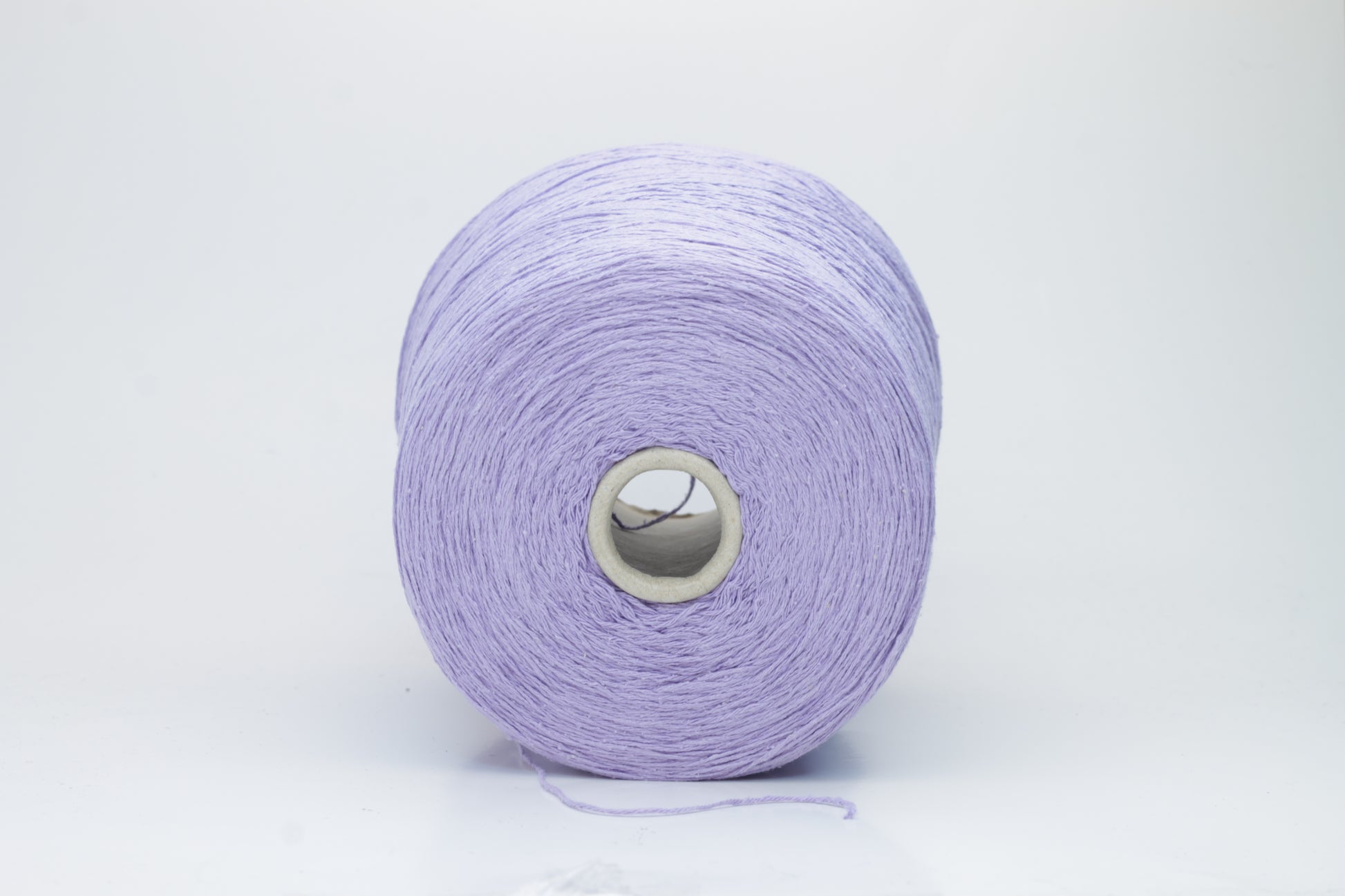 Close-up of a single strand of matte lavender silk bourette yarn, showcasing its natural slub texture and soft, nubbly appearance, coiled gently.