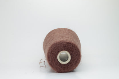 Close-up of fluffy Marrone kid mohair and silk blend yarn, subtly lustrous with a soft halo, gently twisted into a fine, delicate thread.